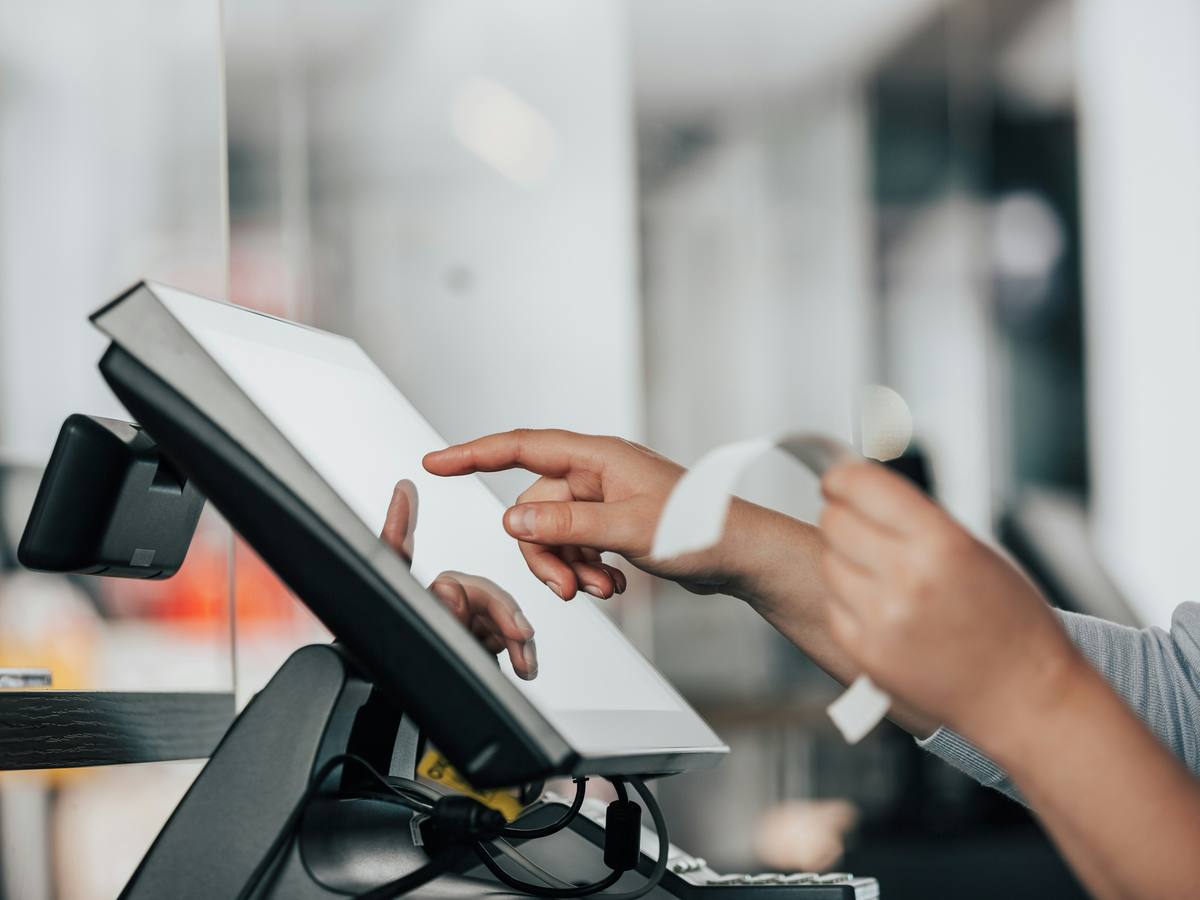 A cashier's hands on a point of sale screen, holding a printed receipt